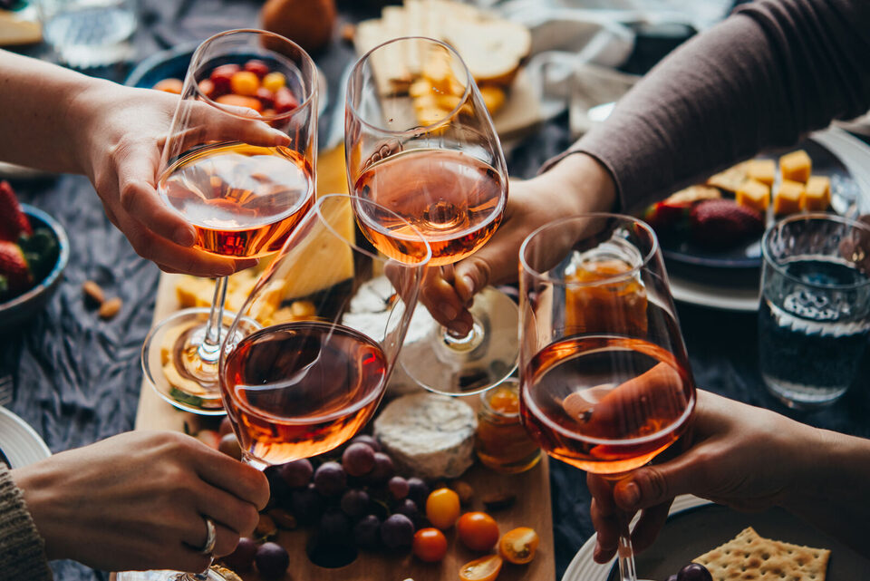 Hände stoßen mit Rosé-Gläsern über einer gedeckten Tafel an