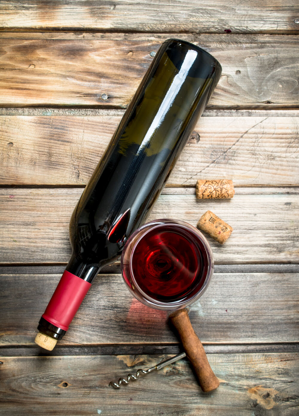 Bottle of red wine with glass and cork on wood