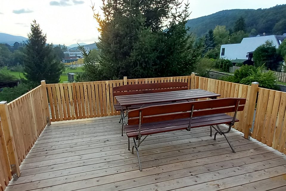 Die Terrasse der Gästewohnung mit Tisch und Bänken, dahinter die Hügel